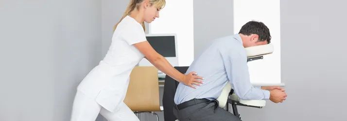 Practitioner performing a seated massage treatment on an individual using a portable massage chair.